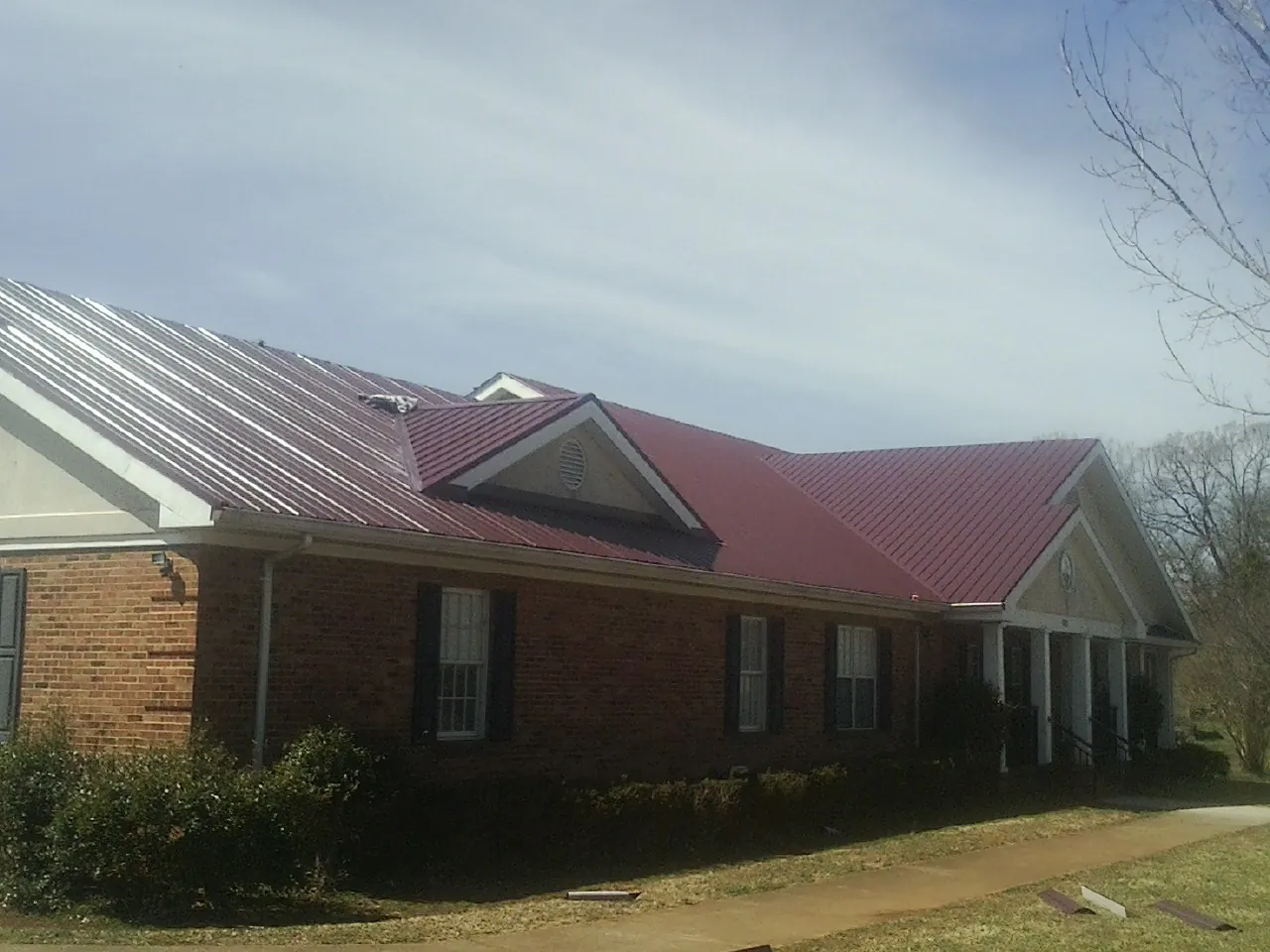 Red metal roof with gabled entries on a long brick building, from a Hail Damage Roof Repair job in Clontarf