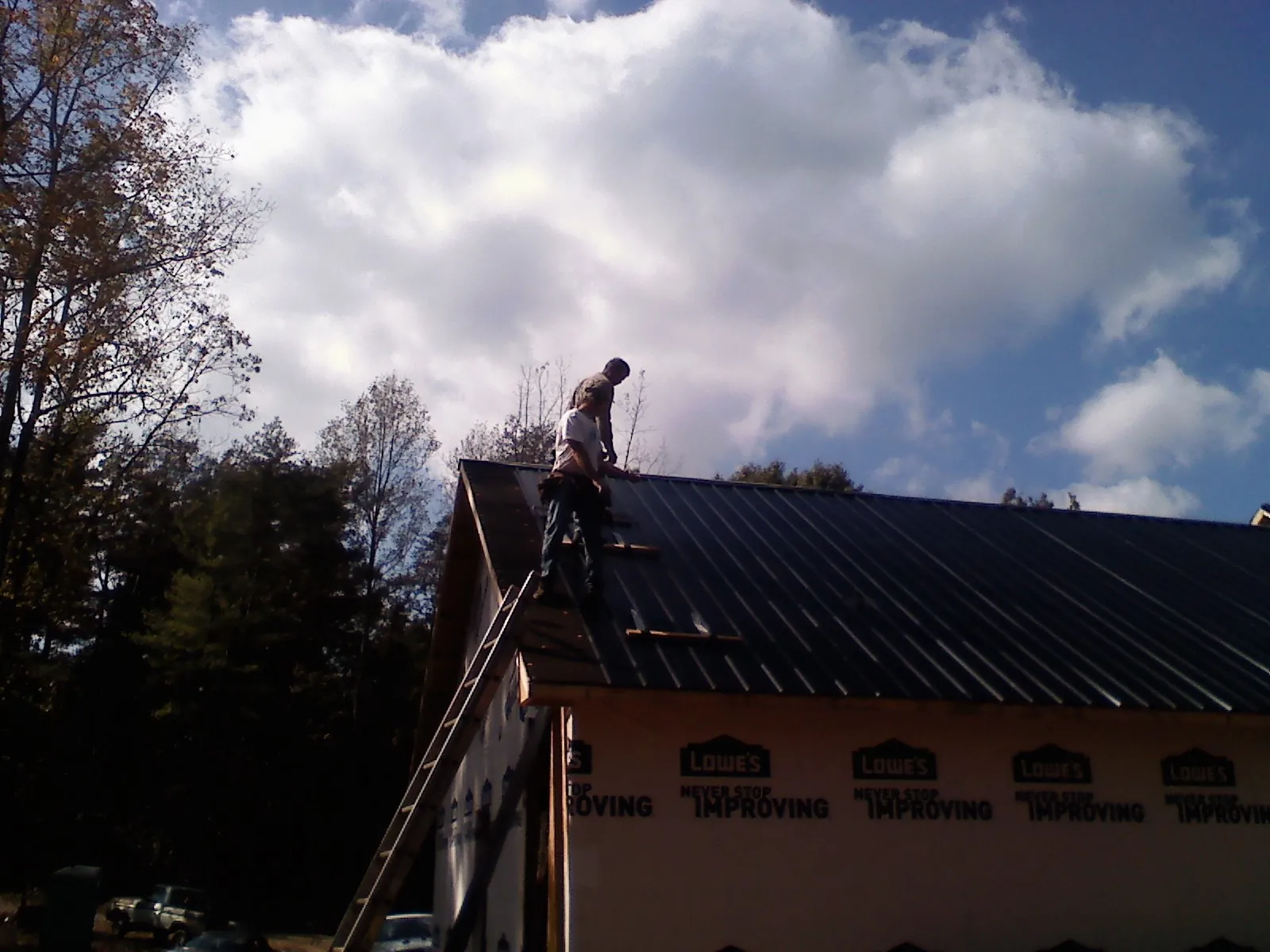 Roofer fastening dark metal panels high against a cloudy sky, from a Roof Inspection job in Clontarf