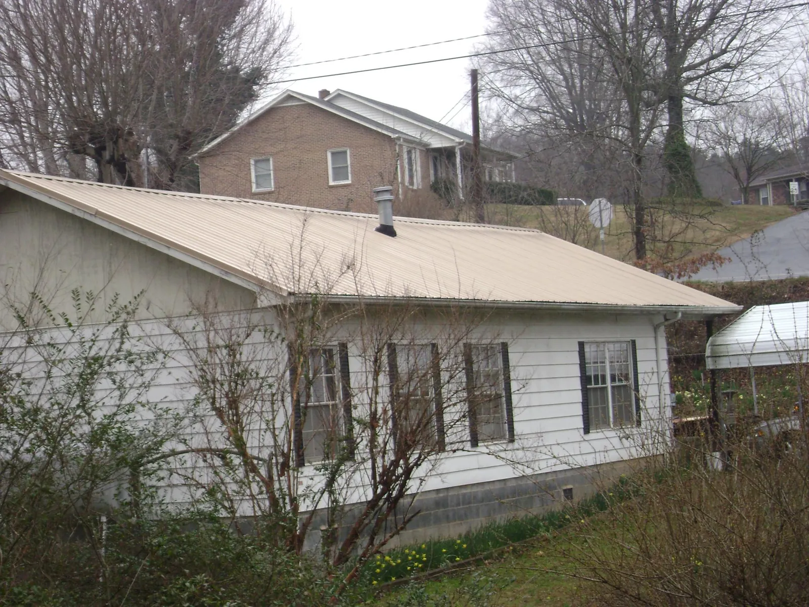 Tan metal roof on a white sided house set into a hillside — Commercial Roofing by Roofing Brothers in Clontarf
